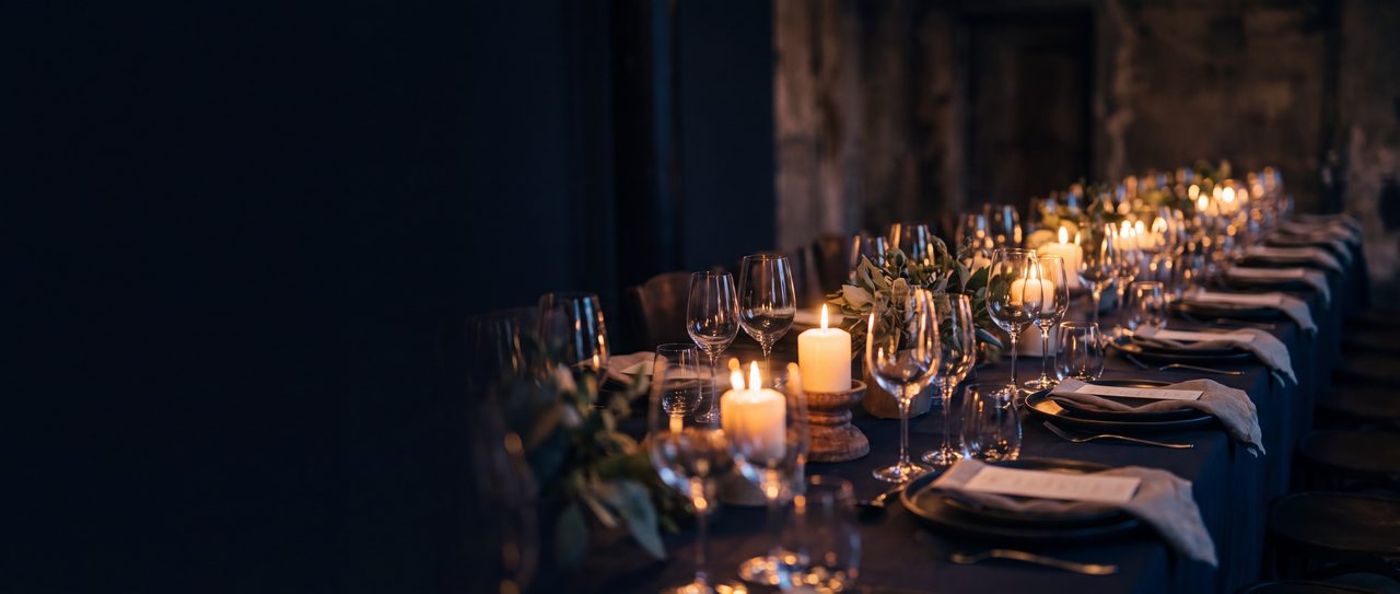 Low candles and glassware down a long table laid for a private event.