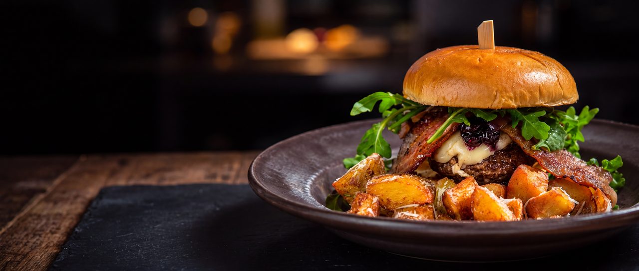 The Bleuberry Royale Burger on a dark ceramic plate against a dark dining room.