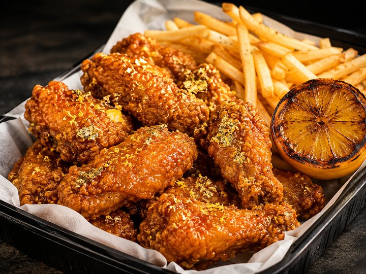 Golden Pepper Wings in a bright golden glaze with lemon zest and a charred lemon half, served with fries.